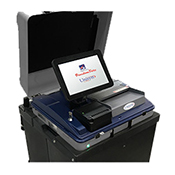 Unisyn FVS thumb Black scanner with white touch screen reading "FreedomVote. Unisyn." Scanner has gray ballot slot and small black receipt printer below screen. Base of scanner is black.