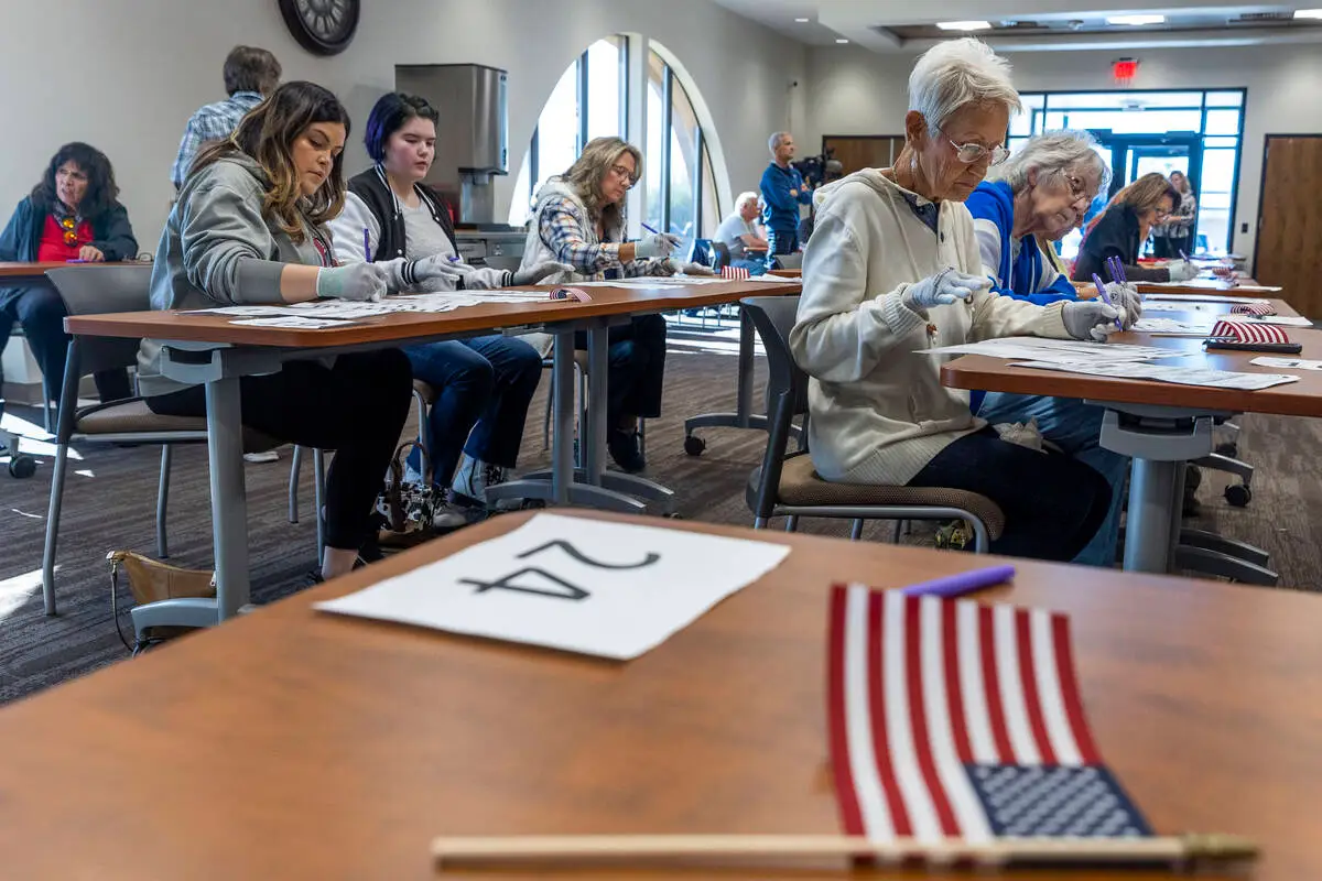 Nye_hand count Volunteers seated at tables hand counting ballots in Nye County at the Valley Conference Center. American flag on desk in forefront